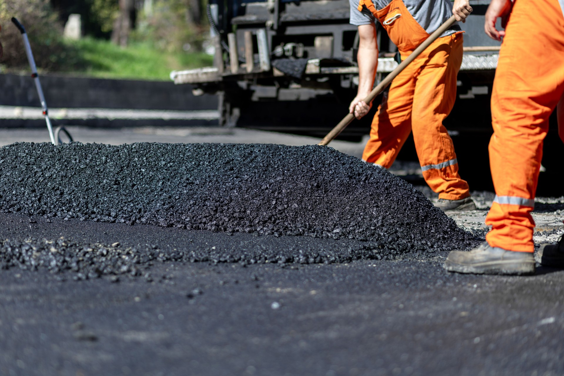 Workers laying asphalt on a road construction site during daylight hours, focusing on creating a smooth surface for vehicles
