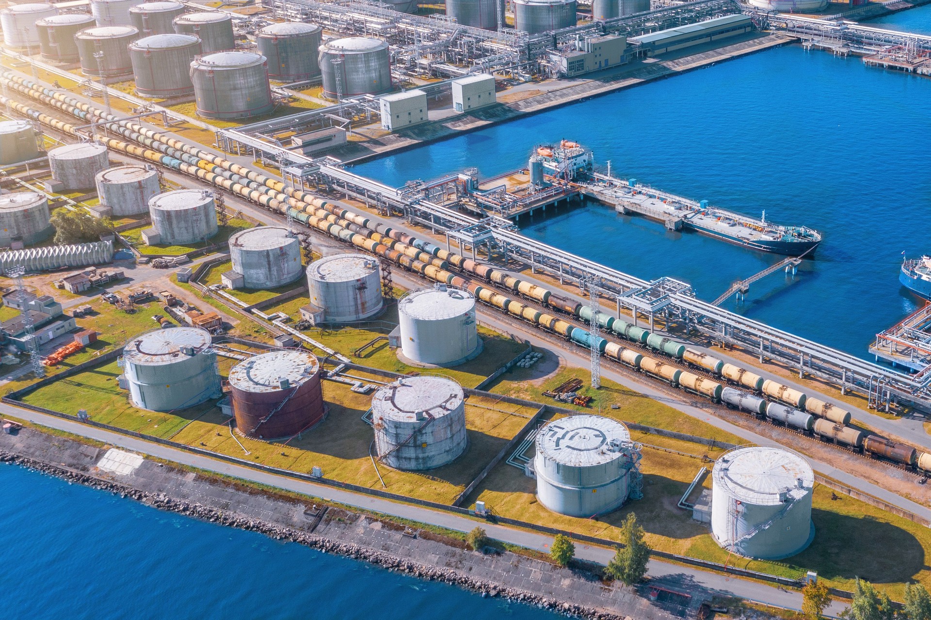 Aerial view large port oil loading terminal with large storage tanks. Railway infrastructure for the delivery of bulk cargo by sea, using pump station in ship tanker for transportation and delivery.